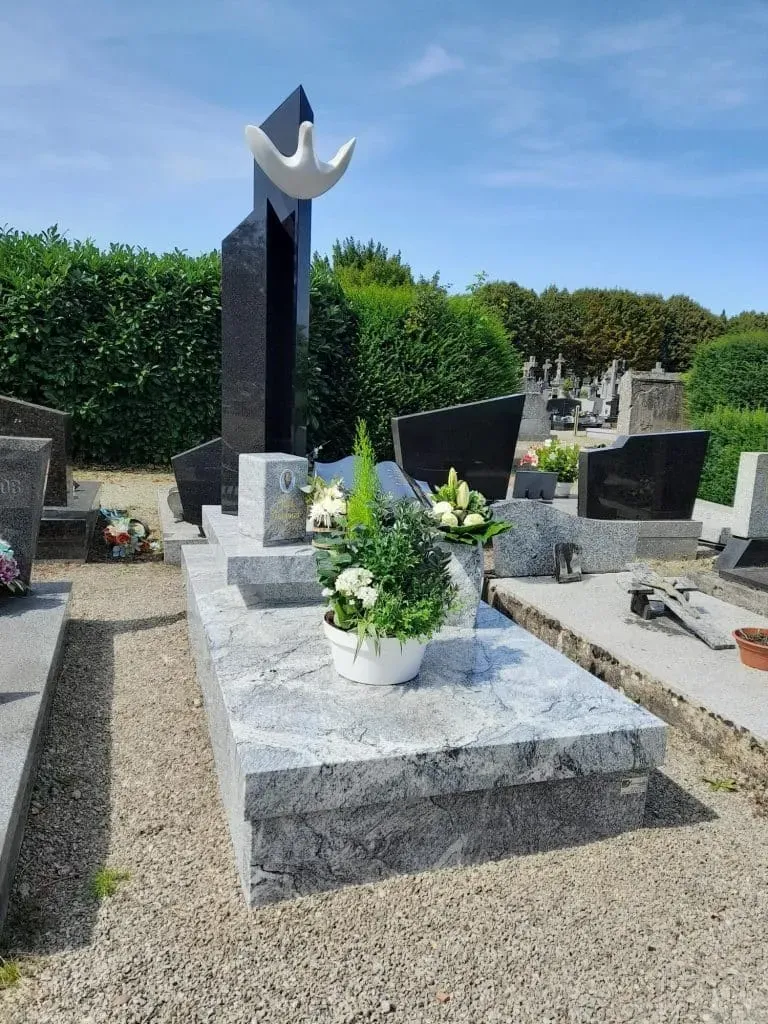 Tombe moderne en granit gris ornée d'une sculpture d'oiseau blanc.